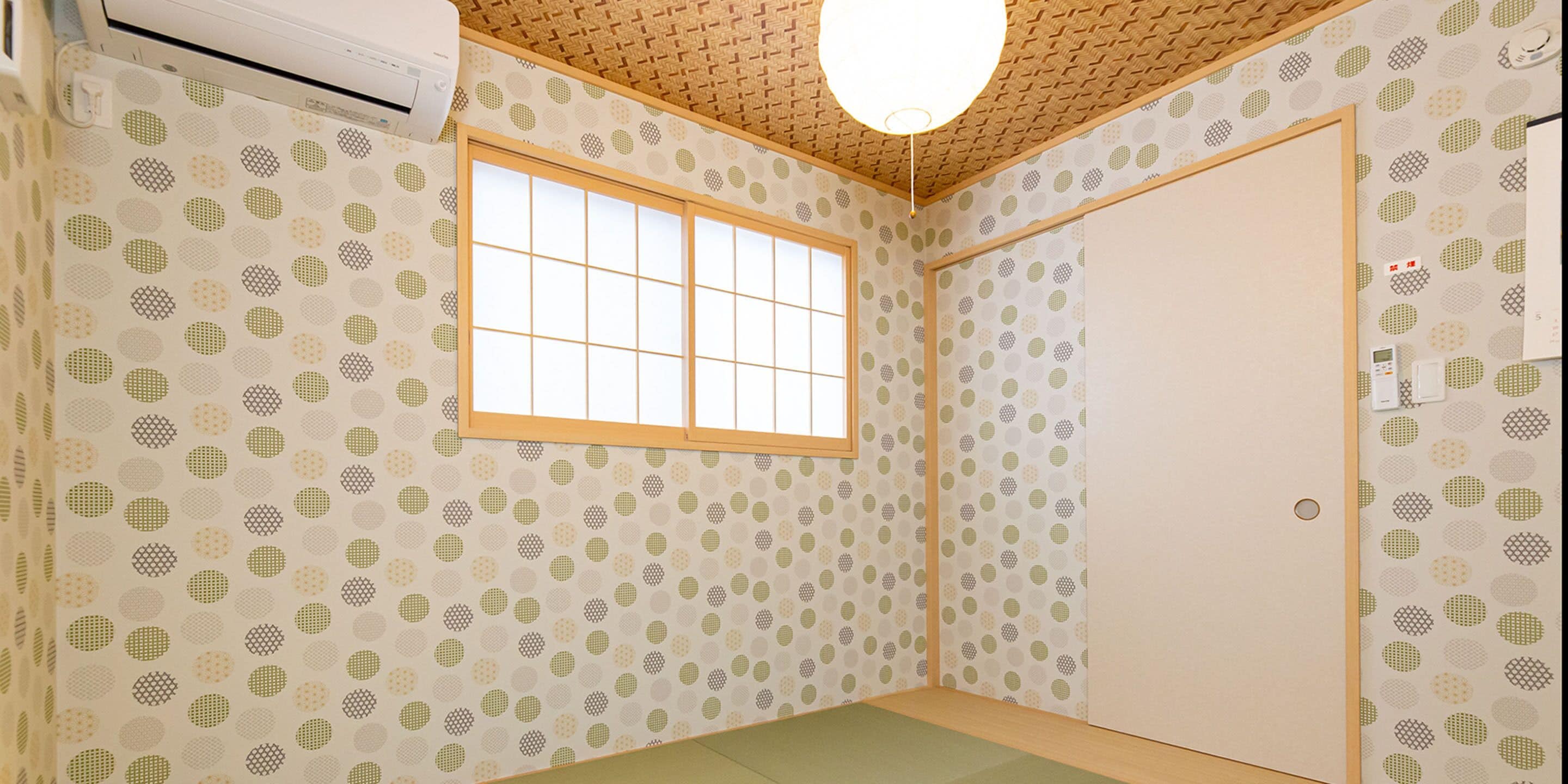 Ein Zimmer mit gestreiftem Wandpapier, einem Fenster mit Holzrahmen, einer Tür und einer Deckenleuchte.