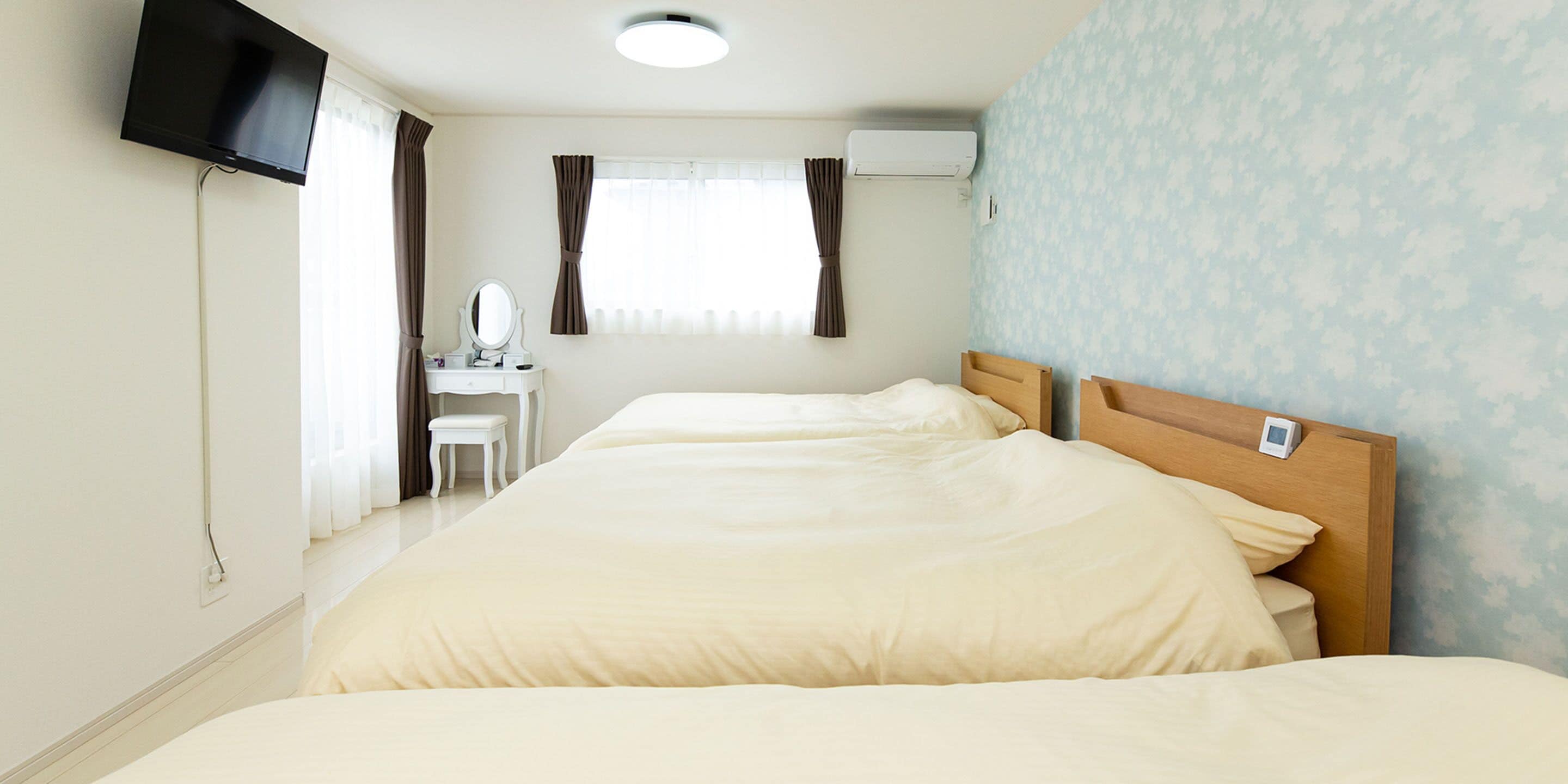 Quarto de hotel com duas camas, uma escrivaninha com espelho e uma televisão fixada na parede.