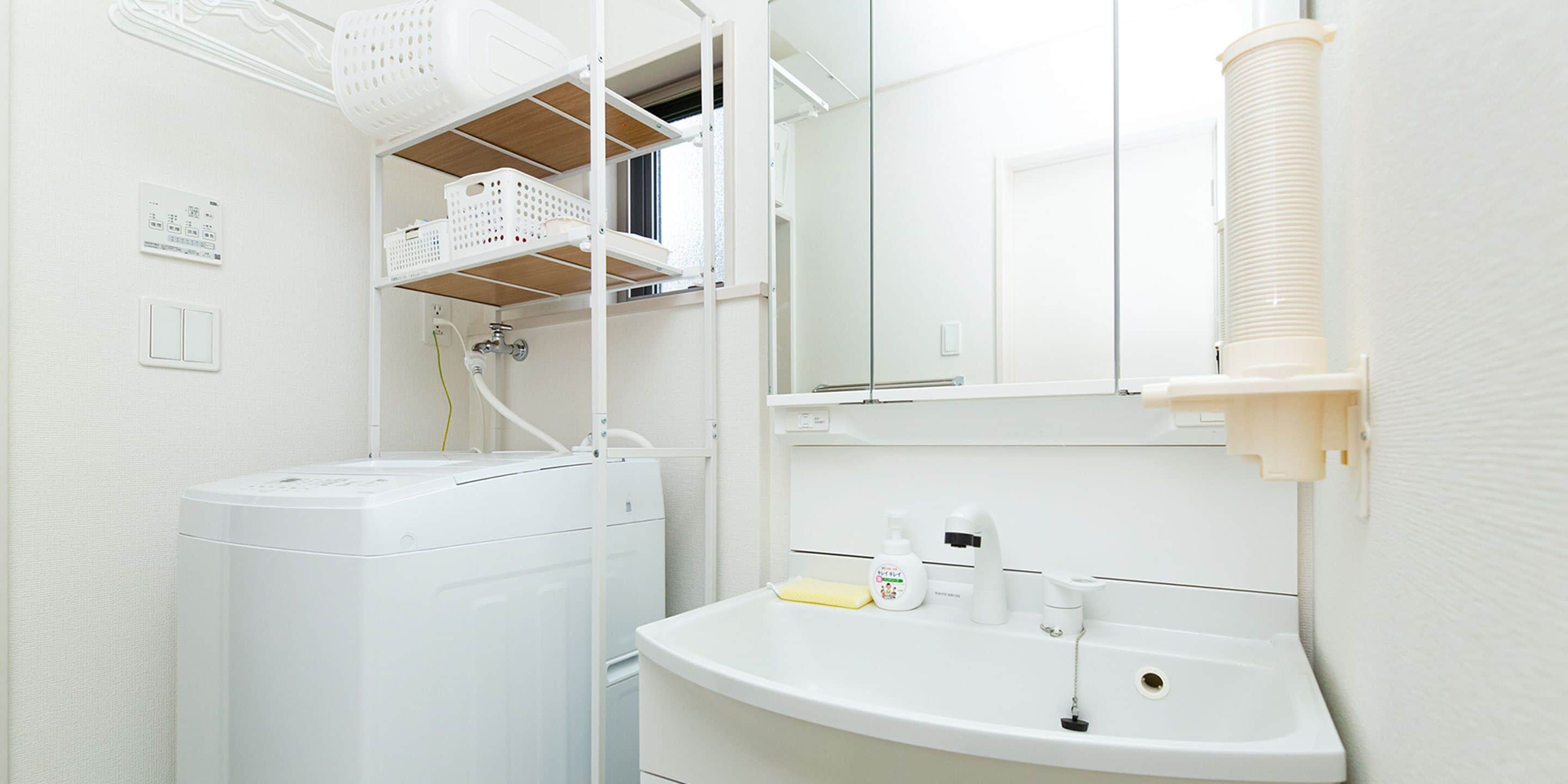 A compact, modern bathroom with a built-in washing machine, a sink with a mirror, and a shelf with baskets.