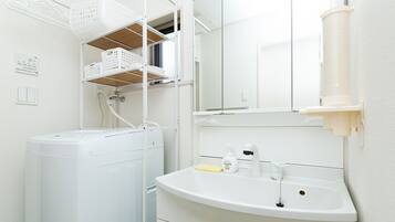 A compact, modern bathroom with a built-in washing machine, a sink with a mirror, and a shelf with baskets.