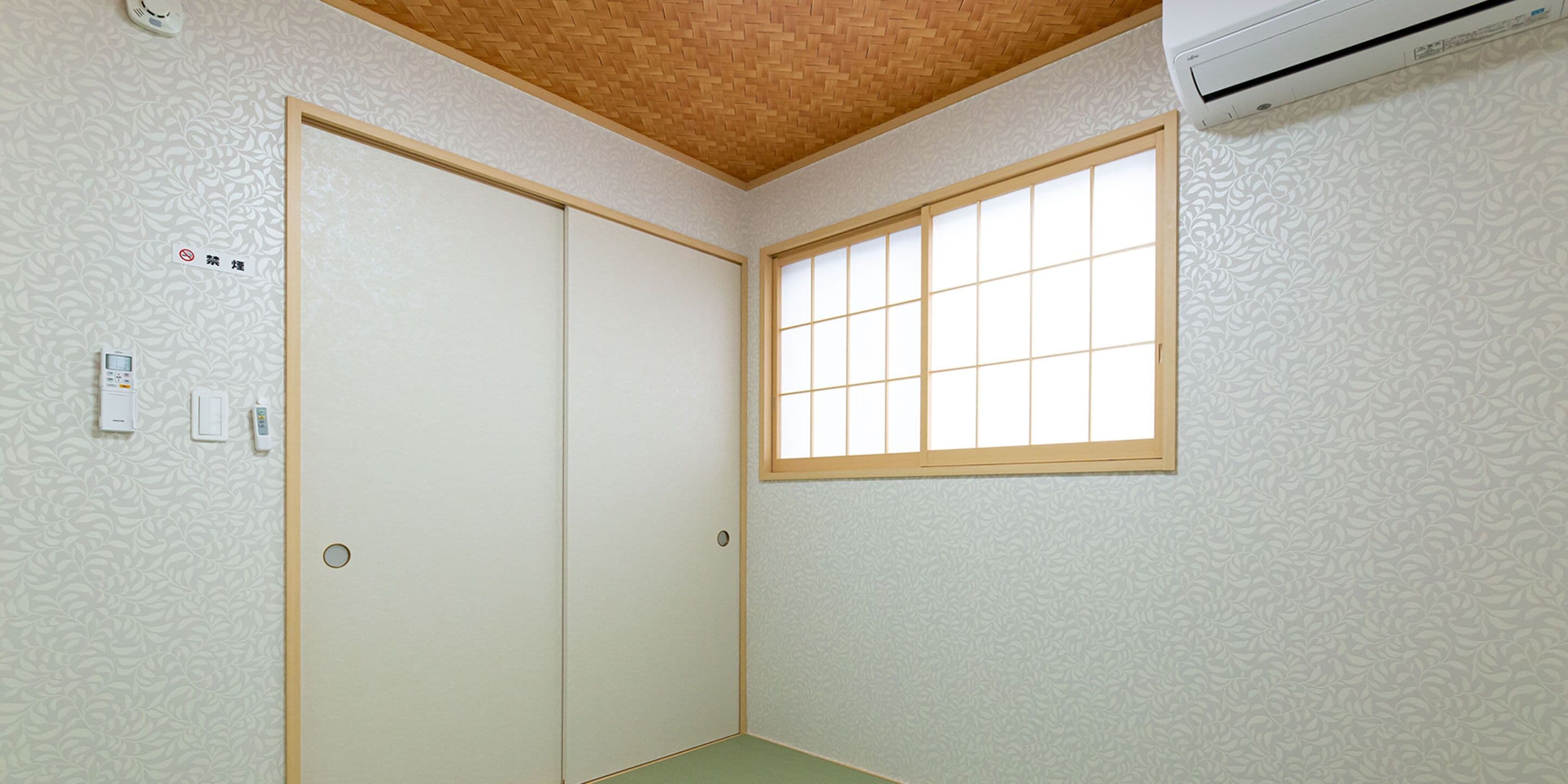 Una habitació amb una porta corredissa, una finestra amb un disseny de reixa i un termòstat a la paret.