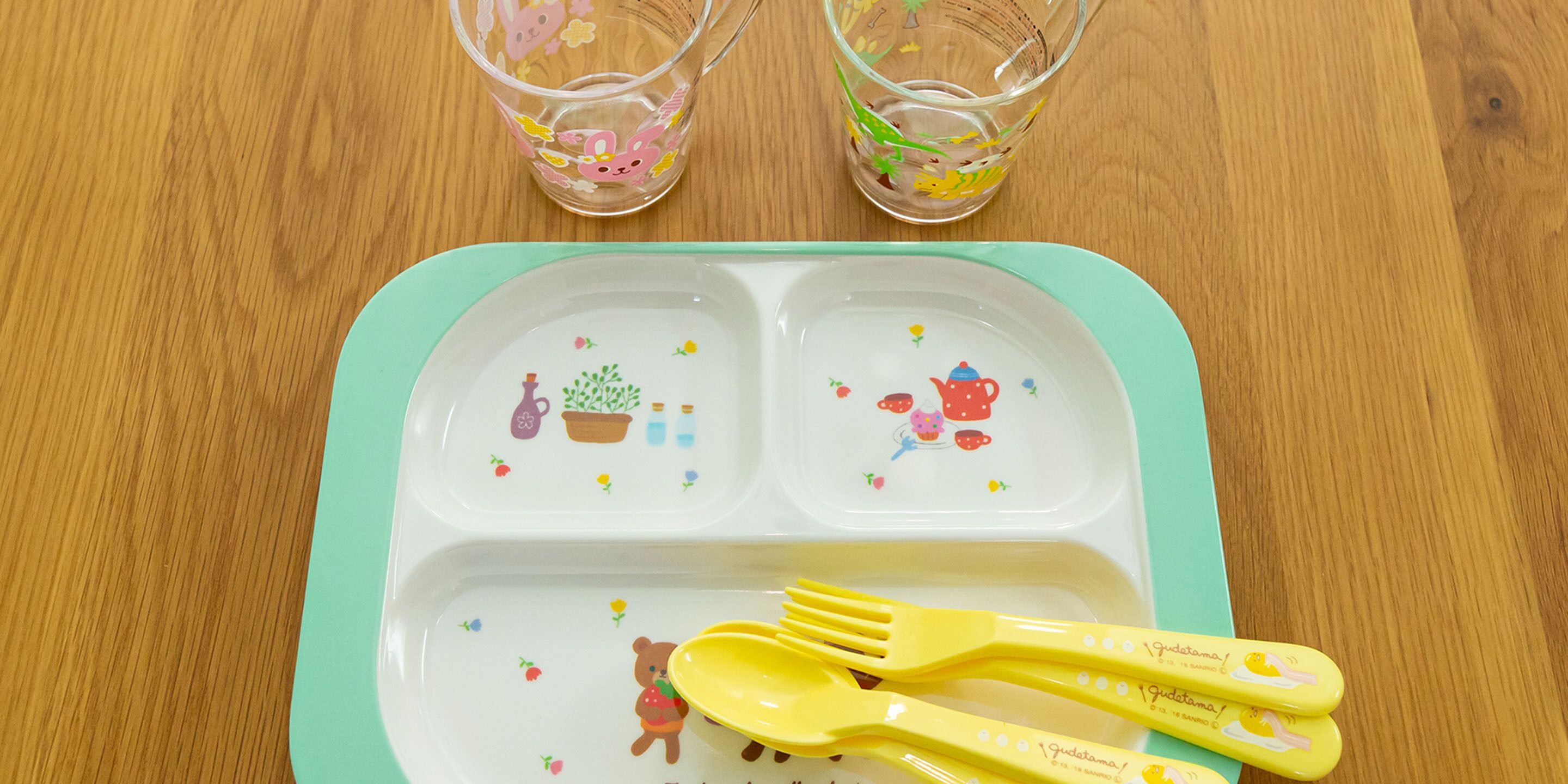 Une table avec un plateau vert, deux verres transparents ornés de motifs floraux et un ensemble de couverts.