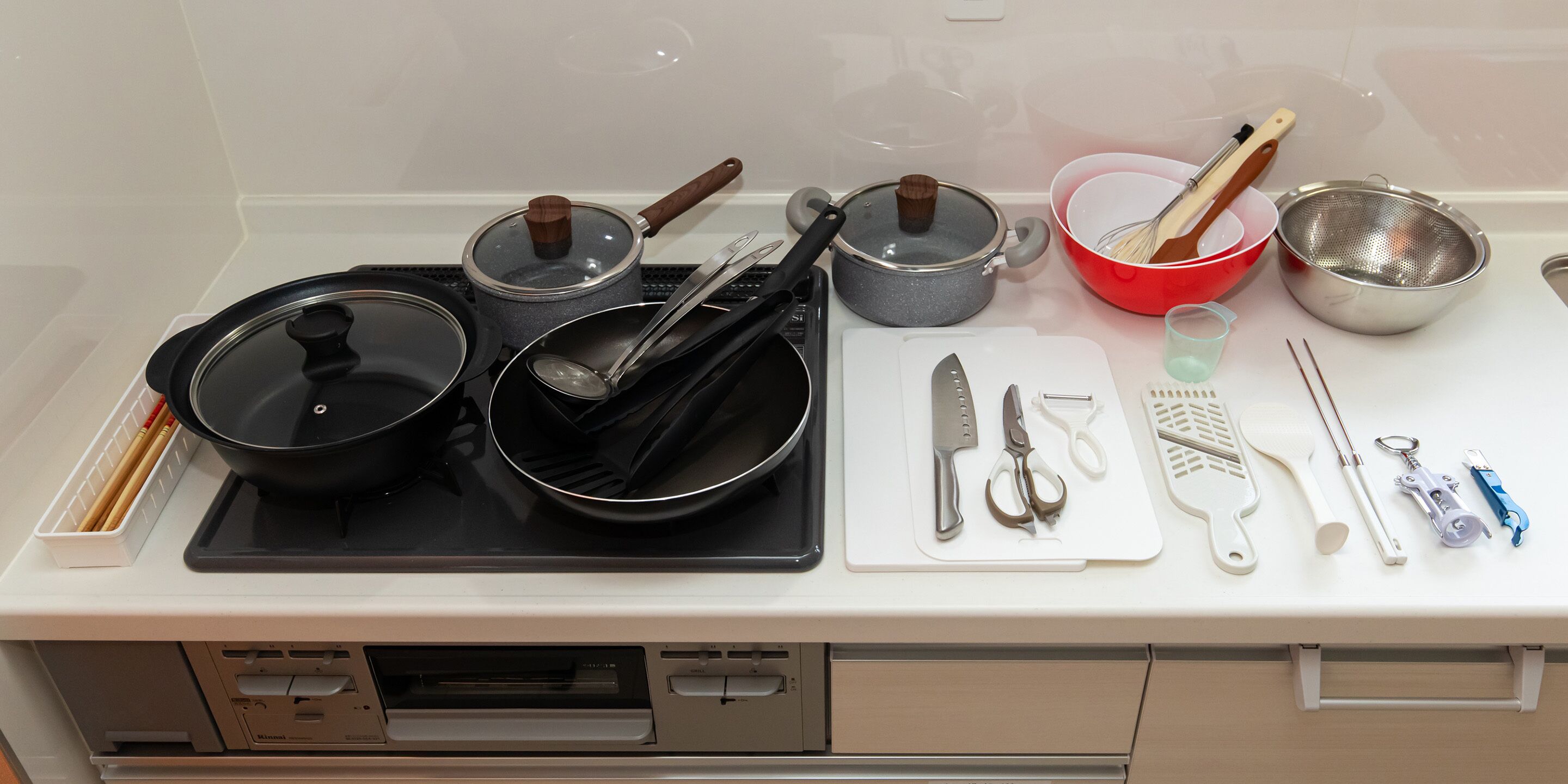 Una encimera de cocina con varios utensilios y electrodomésticos, como ollas, sartenes, una tabla de cortar y un juego de cuchillos.