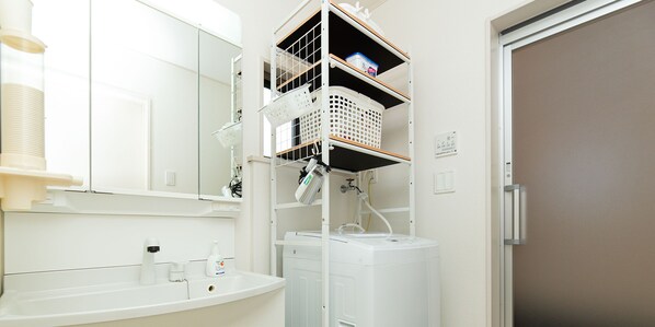 A bathroom with a white sink, mirror, and a white washing machine. There are shelves above the washing machine with baskets and a towel rack. - Kinugawa Station Front (Nikko)