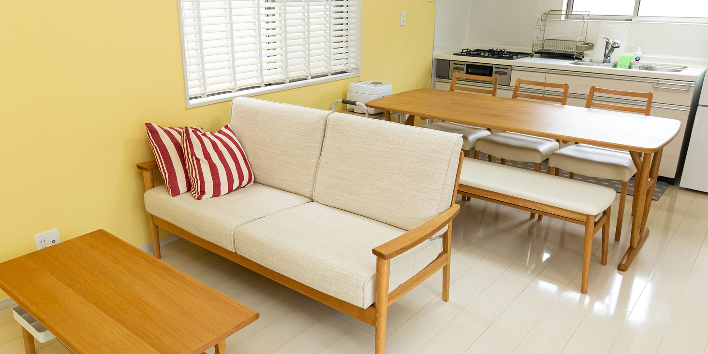 Een compacte woonruimte met een bank, eettafel en stoelen. Achtergrond toont een kitchenette met een fornuis en gootsteen.