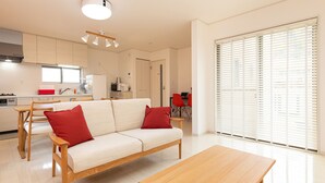 A modern kitchen with white cabinets, a wooden dining table, and a beige sofa with red cushions.