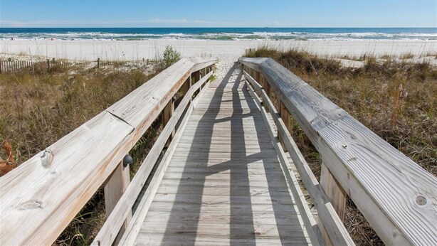 A wooden boardwalk leading to a beach with sand dunes and the ocean in the background.