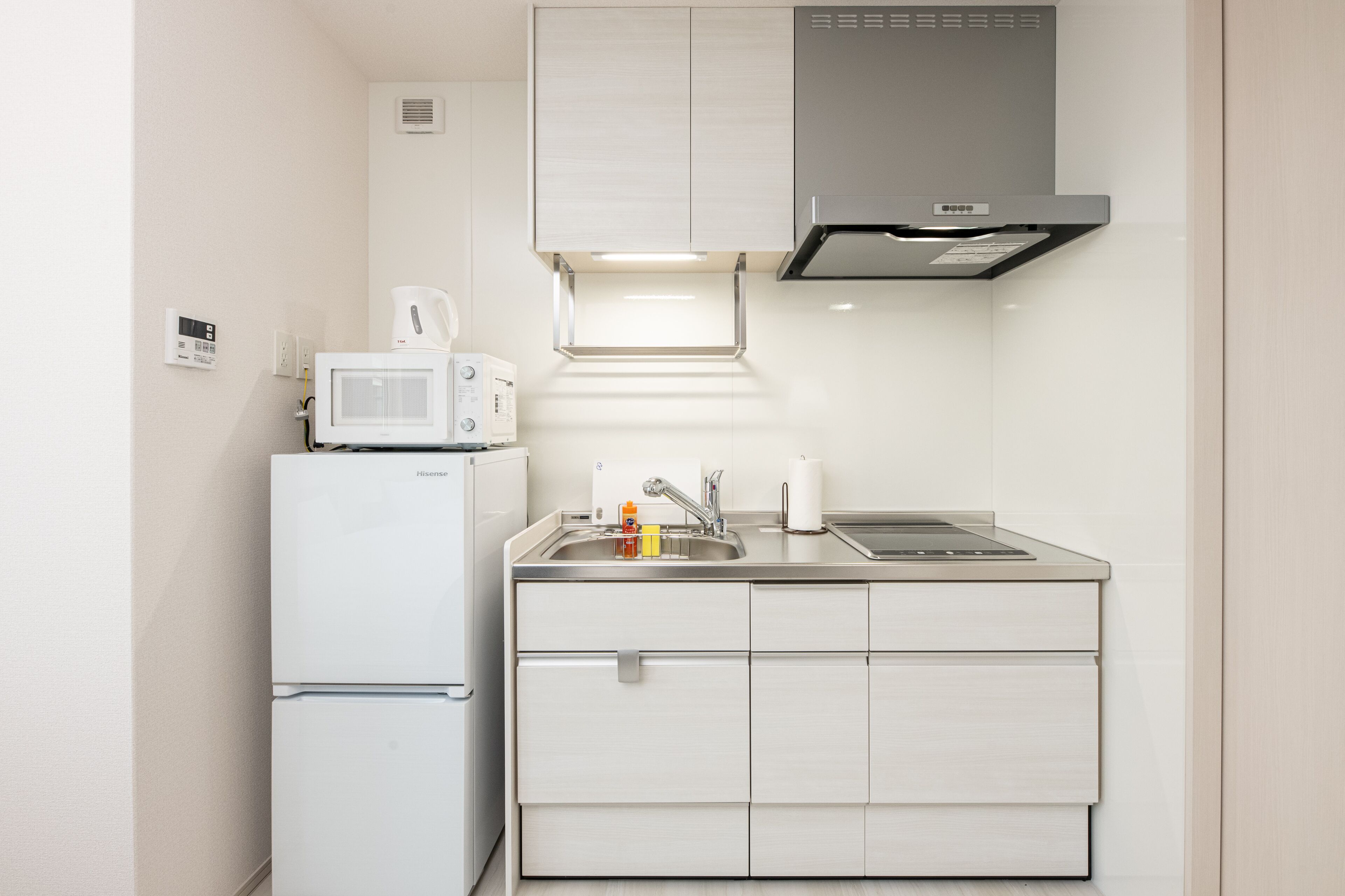 Un angolo cottura compatto con frigorifero bianco, forno a microonde e lavello in acciaio inox.
