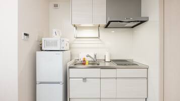 Un angolo cottura compatto con frigorifero bianco, forno a microonde e lavello in acciaio inox.