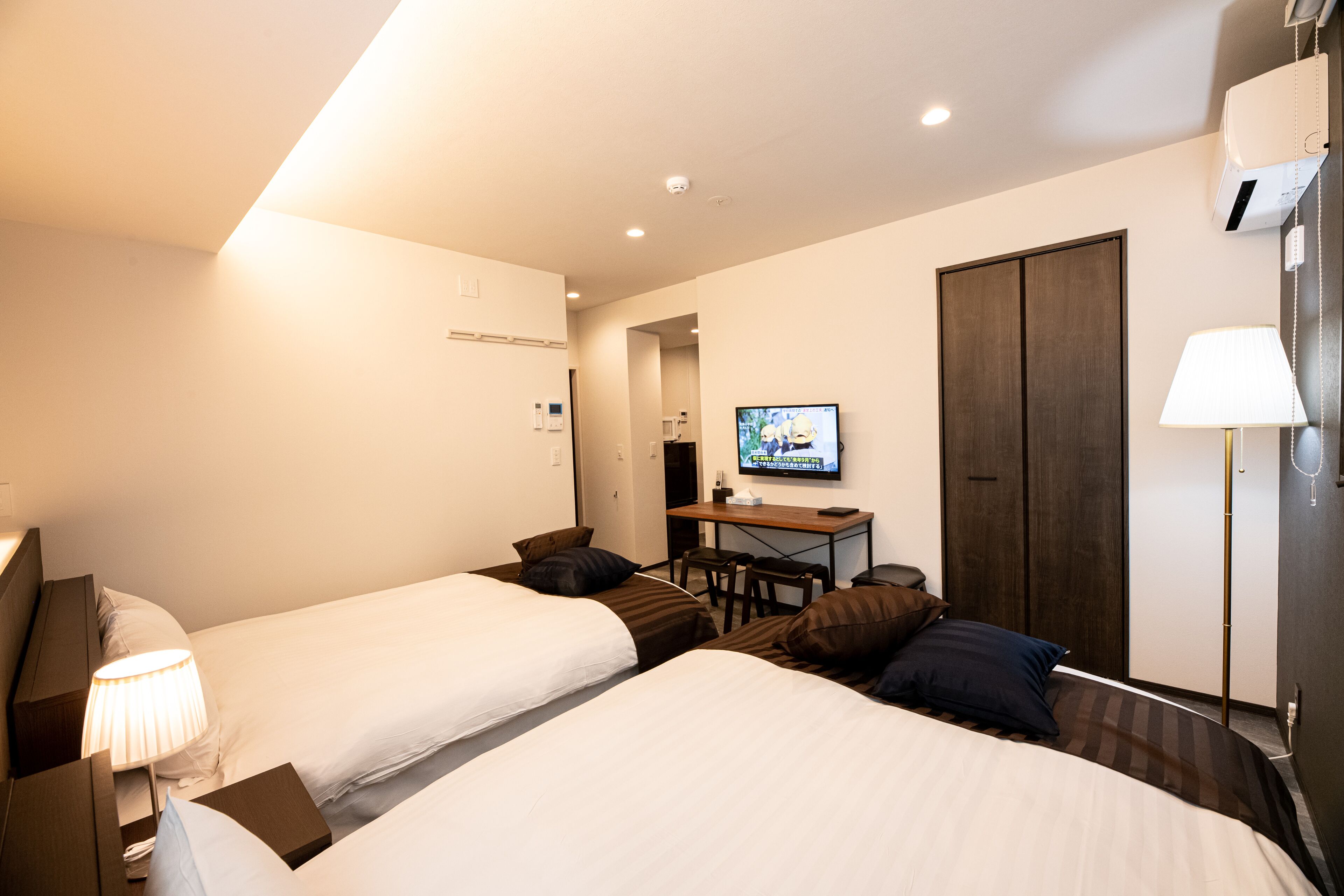 Habitación de hotel con dos camas, un escritorio, un televisor y un armario.