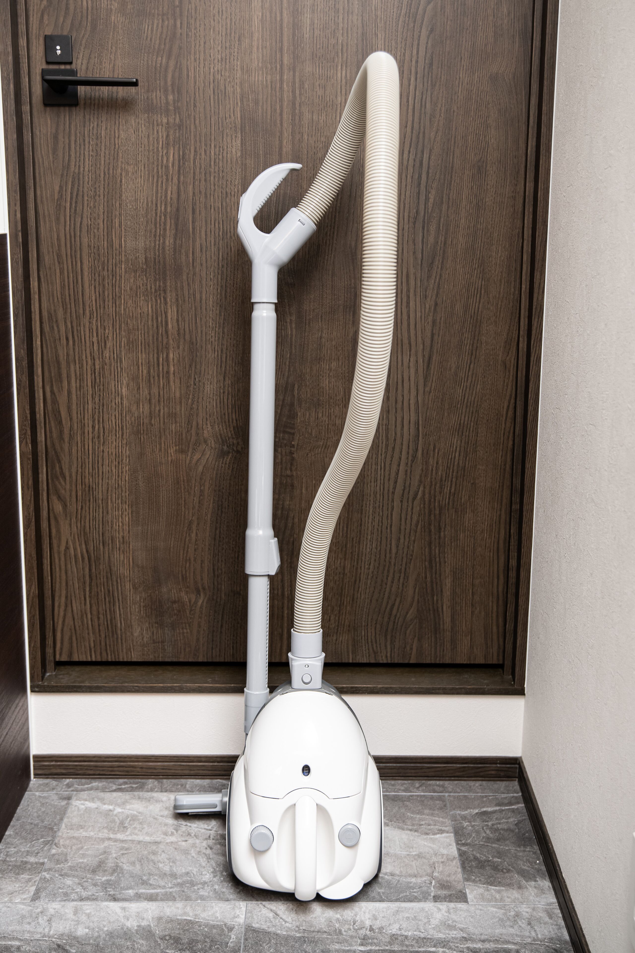A vacuum cleaner in a hallway with a wooden door and tiled floor.