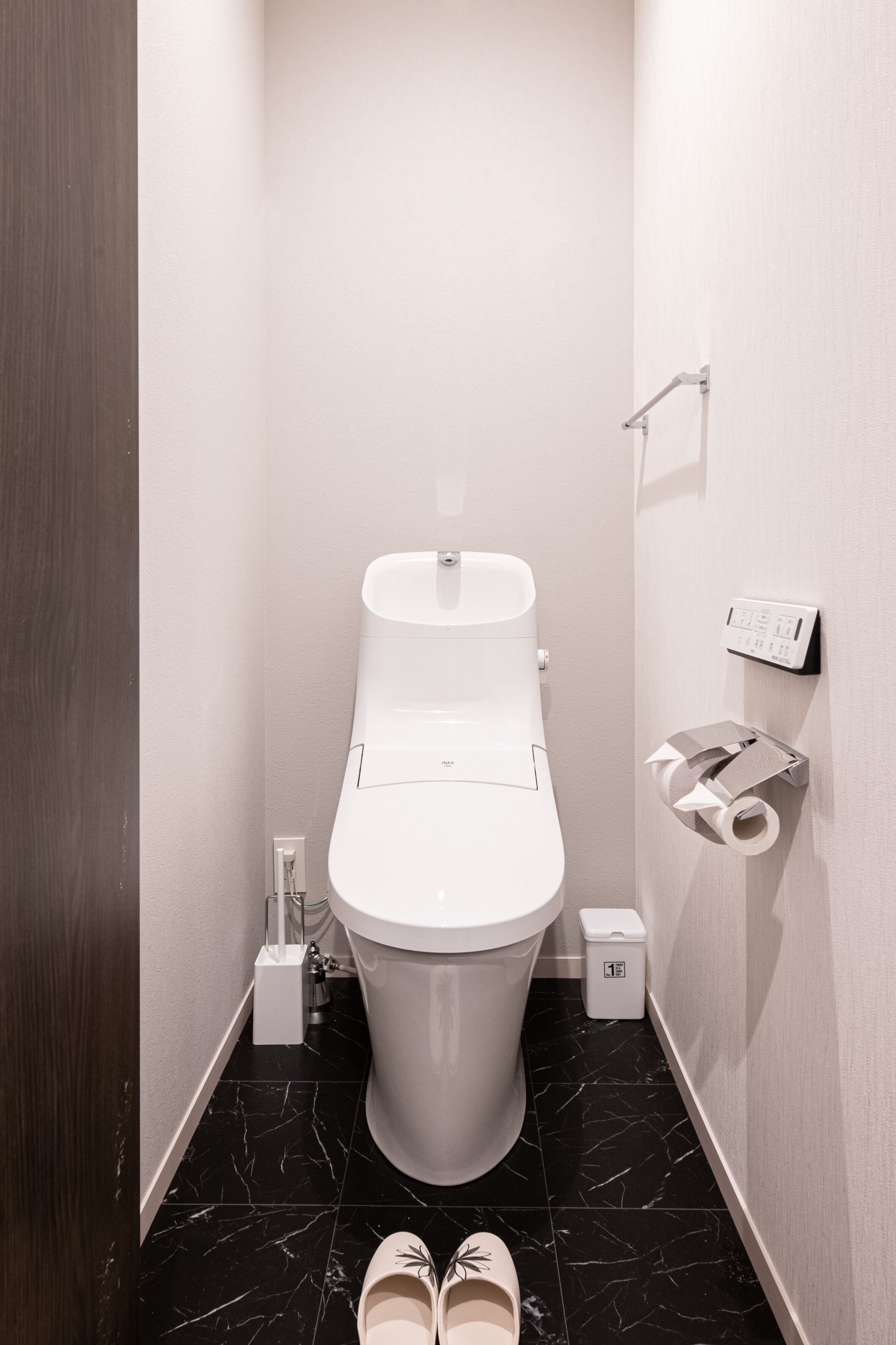 Un baño moderno con inodoro, un cesto de basura y un dispensador de papel higiénico en la pared.