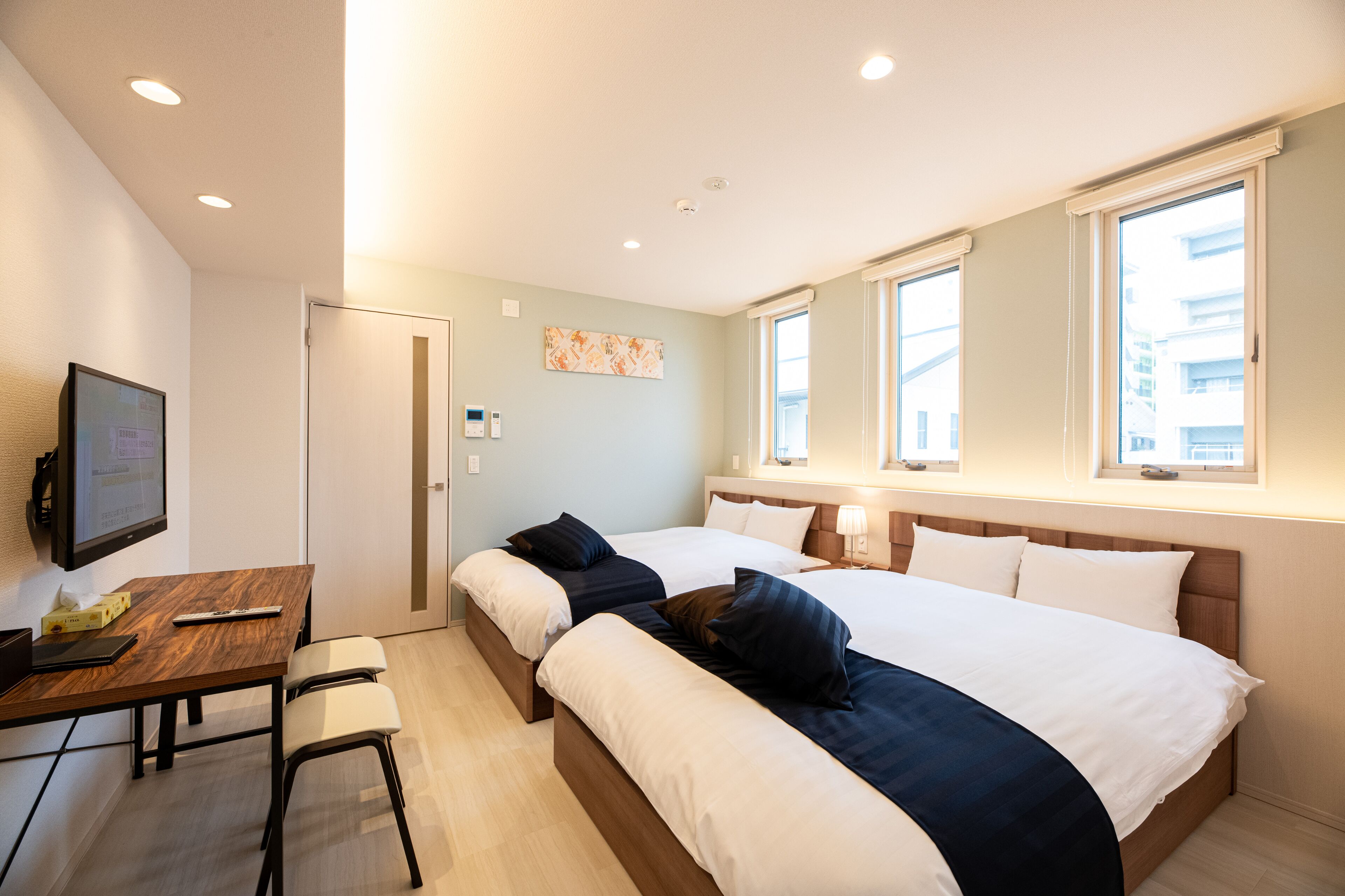 A hotel room with two beds, a desk with a chair, a television, and a window with a view of buildings.