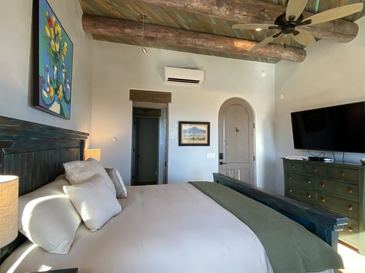 A bedroom with a large bed, a ceiling fan, a television, and a dresser.