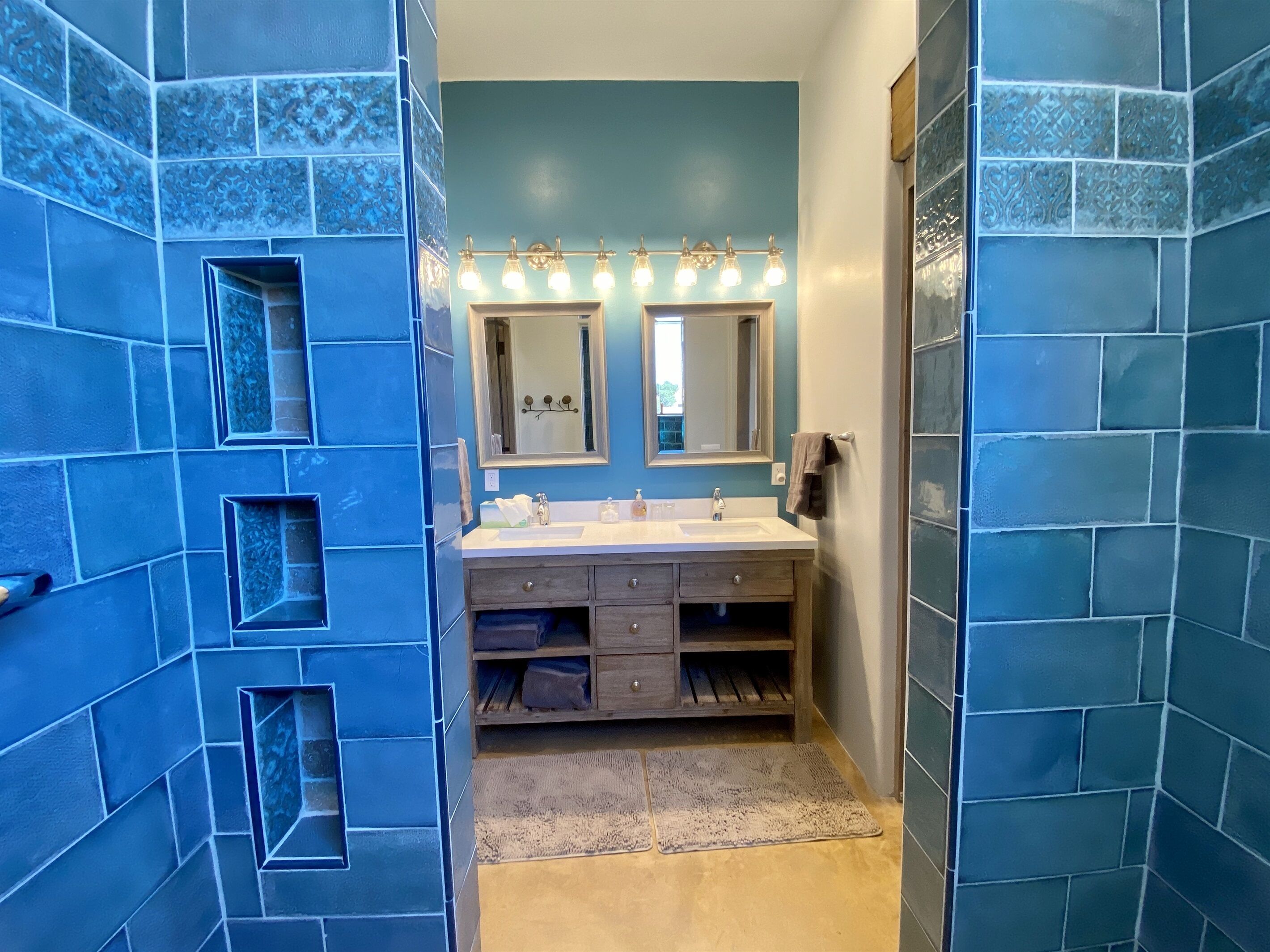 A bathroom with blue tiled walls, a double sink vanity, a mirror, and a towel rack.