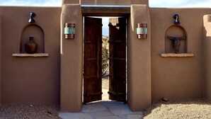 A doorway with a rustic wooden door, flanked by two wall-mounted light fixtures and a bull's head decoration. - Secluded Desert Oasis: Luxurious Inn-Abiquiu Lake Views-Daily Gourmet Breakfast. (Abiquiu)
