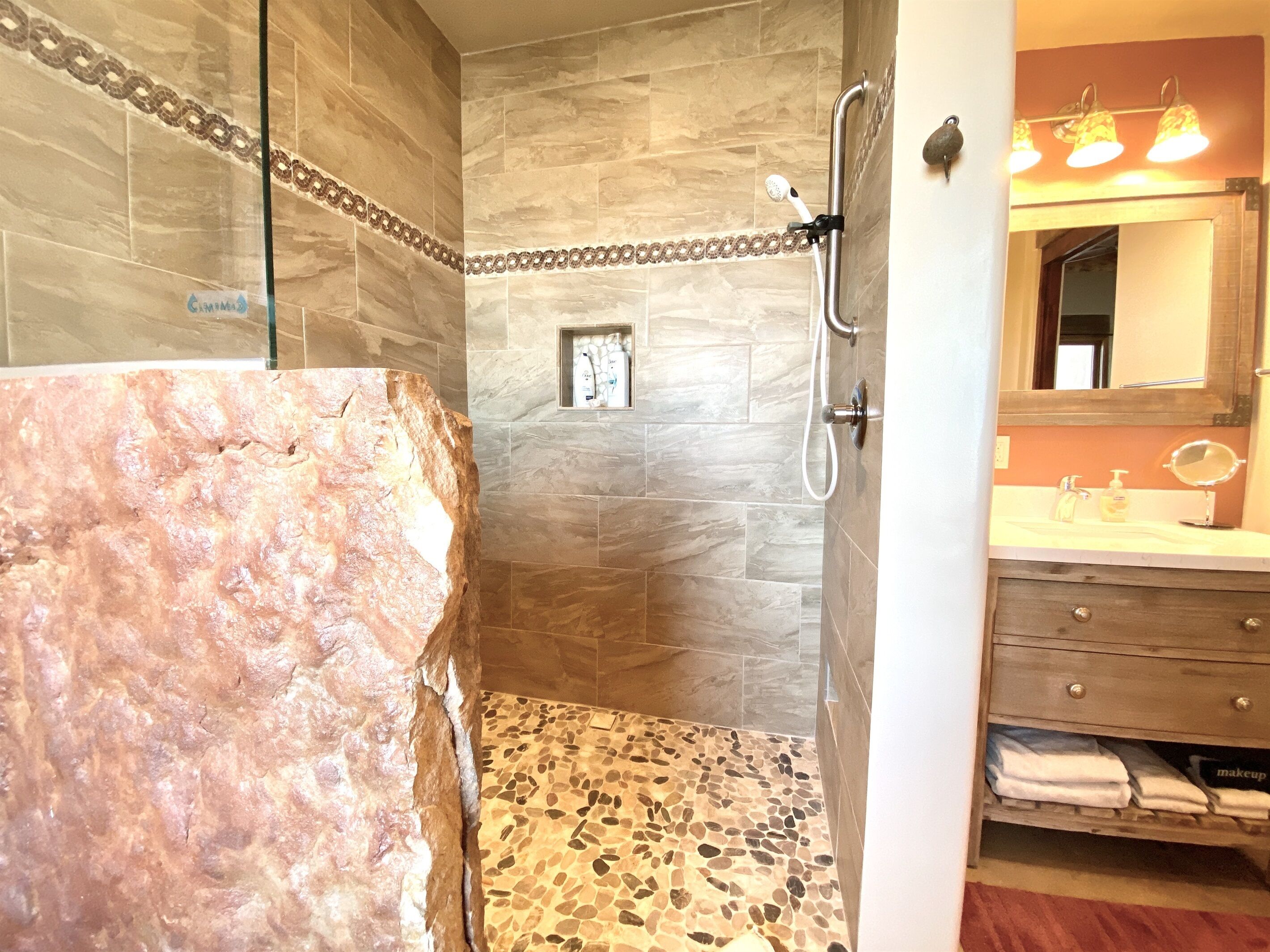 A bathroom with a shower area, a vanity with a mirror, and a towel rack.