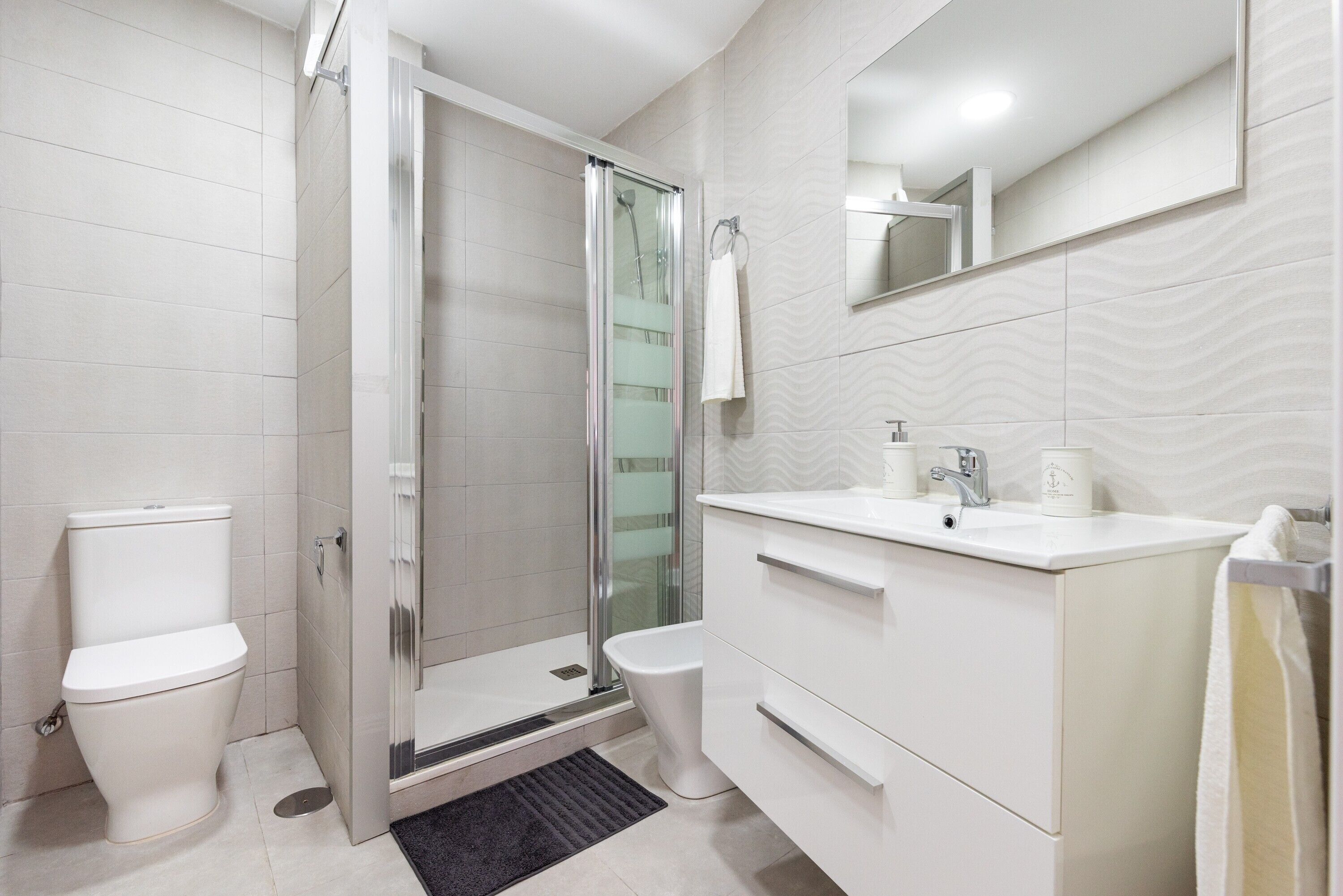 Ein modernes Badezimmer mit einer gläsernen Duschkabine, Toilette, Waschbecken mit Spiegel und Handtuchhalter.