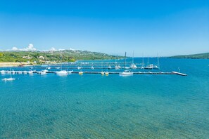 Una marina con barcos amarrados, agua azul cristalina y un paisaje montañoso al fondo.