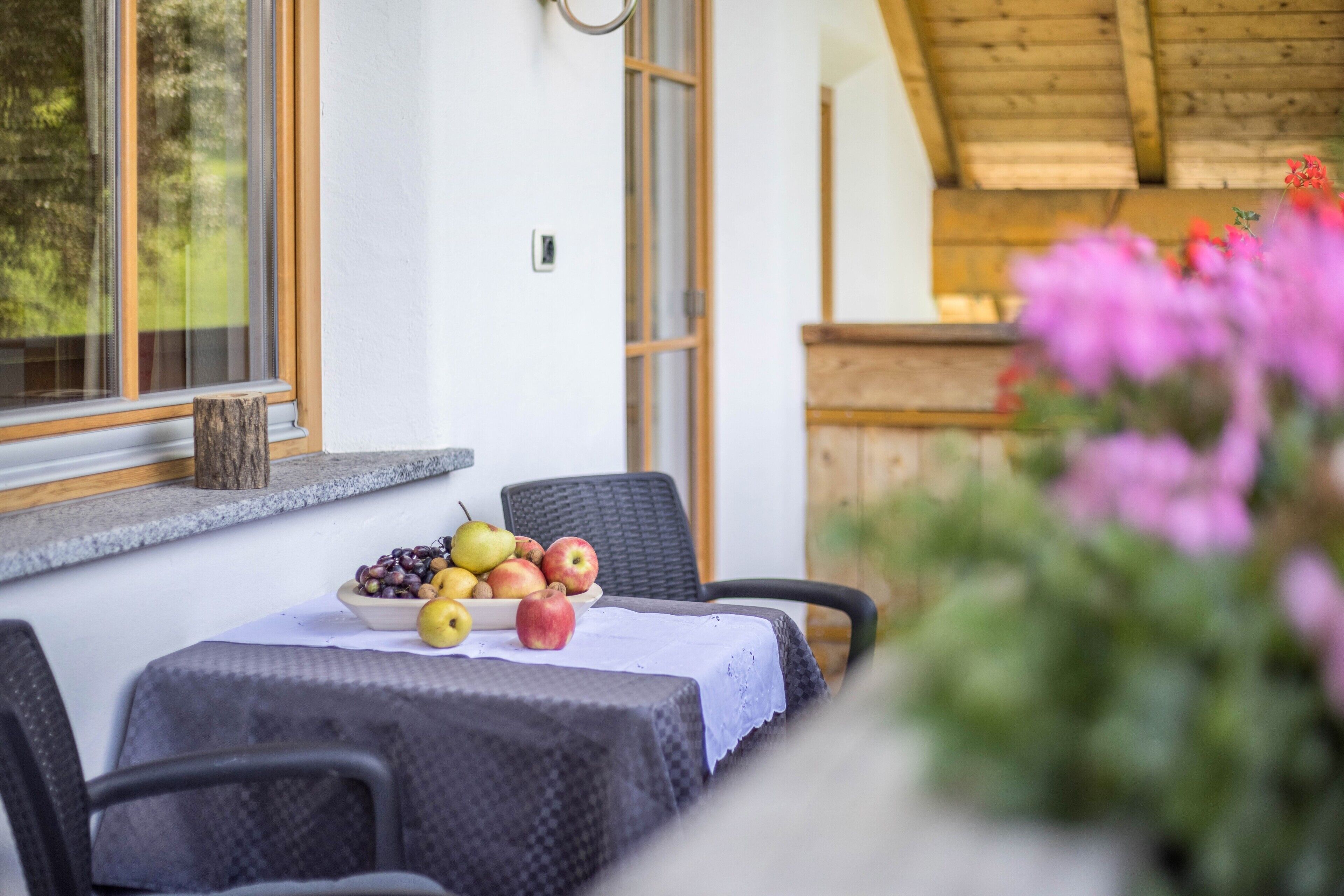 Una mesa con fruta y una silla de mimbre, una ventana y un techo de madera.