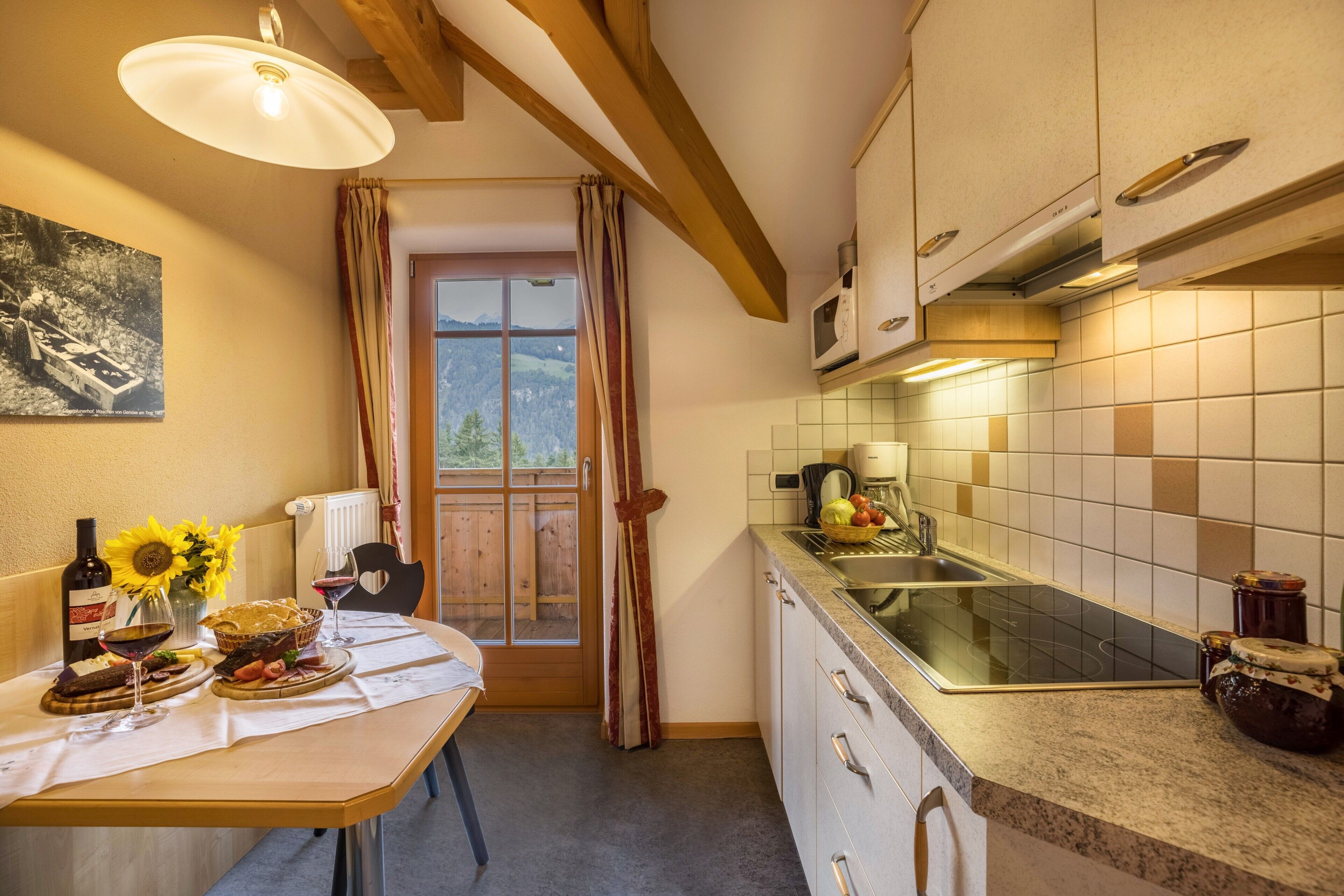 Una cocina con una mesa de madera, una ventana con cortinas, un microondas y un lavabo.