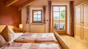Une chambre avec un plafond en bois, une fenêtre avec des rideaux, un lit recouvert d’une couvre-lit à motifs et une armoire.