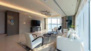 Una sala de estar moderna con un televisor de pantalla plana, un sofá, dos sillones, una mesa de centro y un ventanal con vistas.