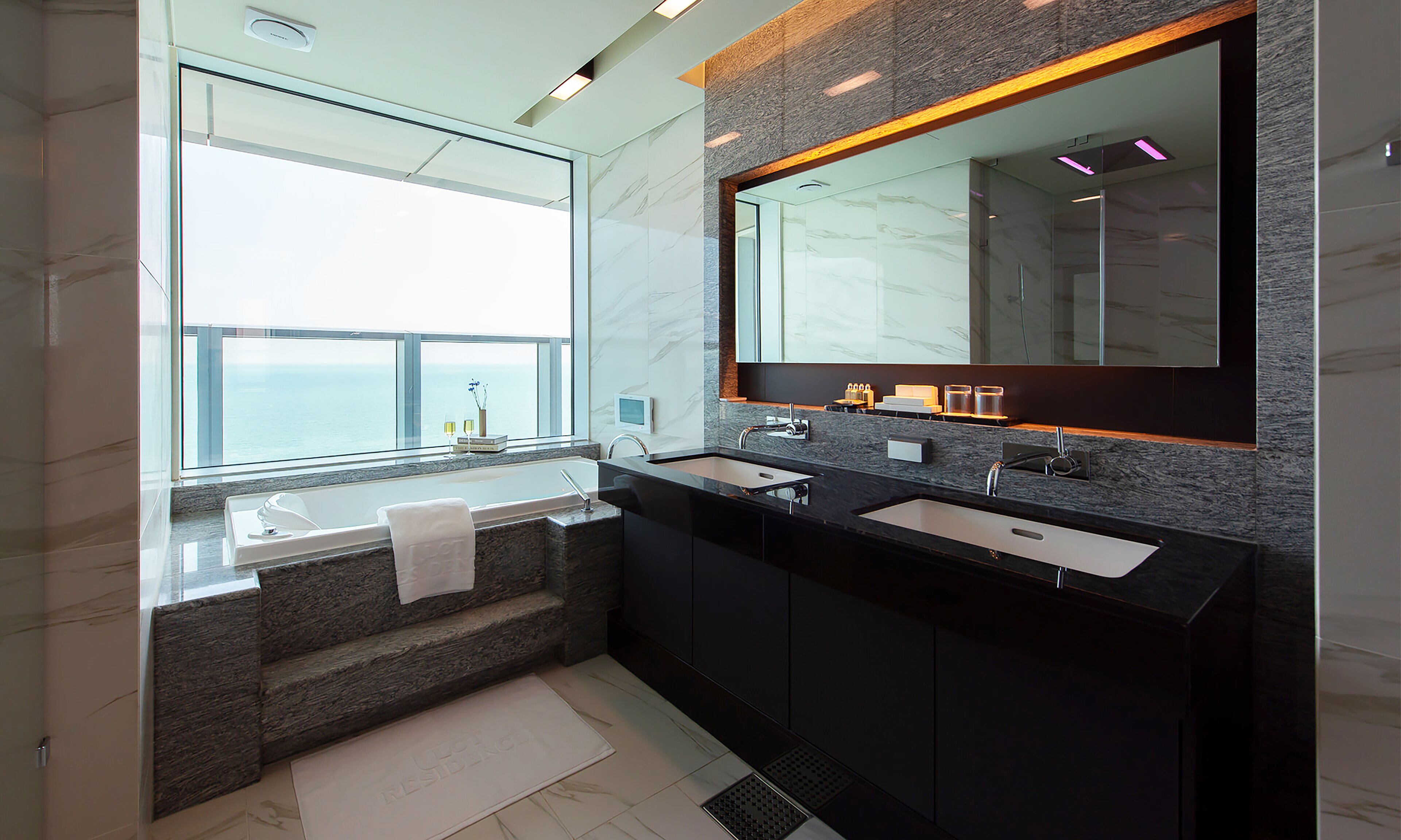 Un baño moderno con un ventanal grande, dos lavabos, una bañera y un espejo.