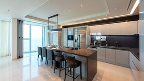 Una cocina moderna con una isla central, taburetes de bar, electrodomésticos de acero inoxidable y un amplio ventanal con vistas.