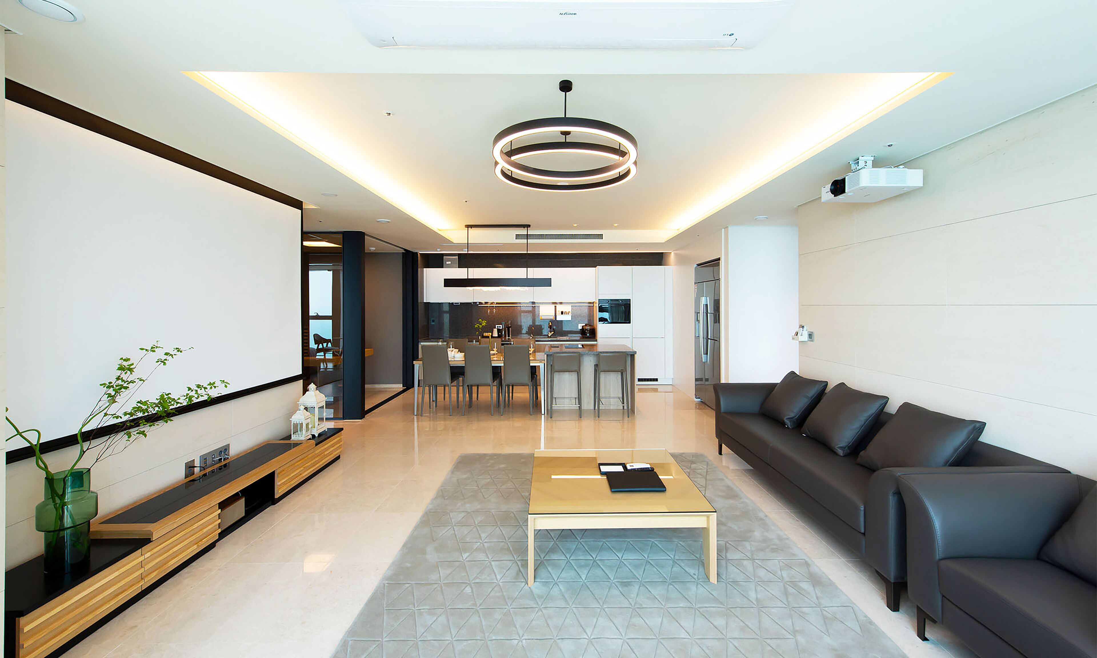 A modern living room with a sofa, coffee table, and a dining area with chairs and a kitchen in the background.