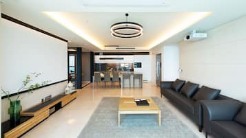 A modern living room with a sofa, coffee table, and a dining area with chairs and a kitchen in the background.