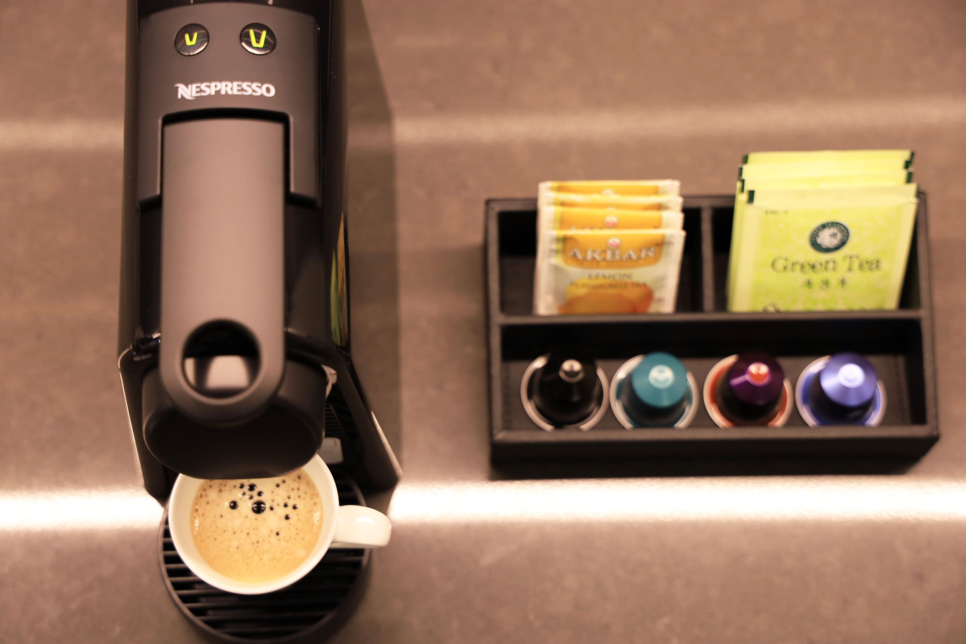 A Nespresso coffee machine dispensing coffee into a cup, with coffee pods and capsules in the background.
