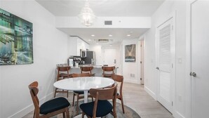 A modern dining area with a round table and wooden chairs, a chandelier, and artwork on the walls. - Oceana 201W See gorgeous sunsets! (Treasure Island)