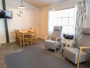 A room with a wooden table and chairs, a sofa, a television, and a window with curtains. - Venuskukkula by Interhome (Äkäslompolo)
