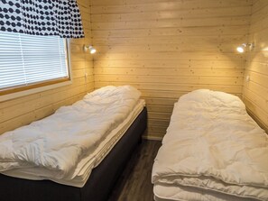 A room with two single beds, wooden walls, a window with blinds, and a wall-mounted light fixture. - Venuskukkula by Interhome (Äkäslompolo)
