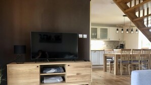 Een moderne woonkamer met een flatscreen televisie, houten meubels en een eethoek met een houten tafel en stoelen.