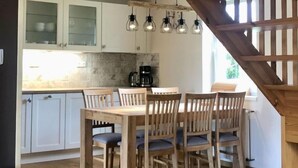 Een keuken met een eettafel en stoelen, houten kastjes, een koffieapparaat en hanglampen.