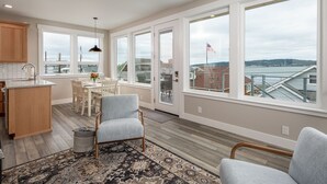 A modern kitchen with large windows, a dining area with a view, and a cozy seating area with a rug. - AC, kayaks, rooftop deck with fire pit, boat launch and incredible views! (Camano)