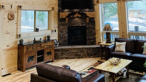 A cozy cabin interior with a stone fireplace, wooden walls, and a large clock.