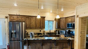 A modern kitchen with wooden cabinets, stainless steel appliances, a granite countertop, and a central island with stools.