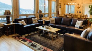 A cozy cabin interior with a large wooden ceiling, a fireplace, a dining area, and a view of the outdoors.