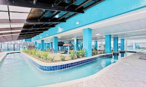 An indoor swimming pool with blue-tiled edges, surrounded by columns and plants.