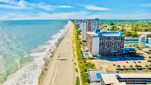 Een kusthotel met meerdere gebouwen, een strand en een parkeerplaats.