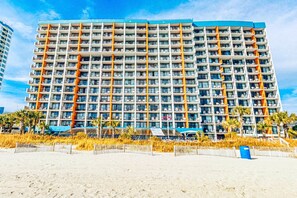 A multi-story hotel with balconies, located near a beach.