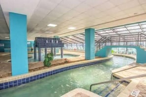 An indoor swimming pool with clear water, blue tiled edges, and a covered area with a roof.