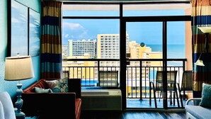 Hotelkamer met balkon, een sofa, een stoel, een tafel en uitzicht op de stad en zee.