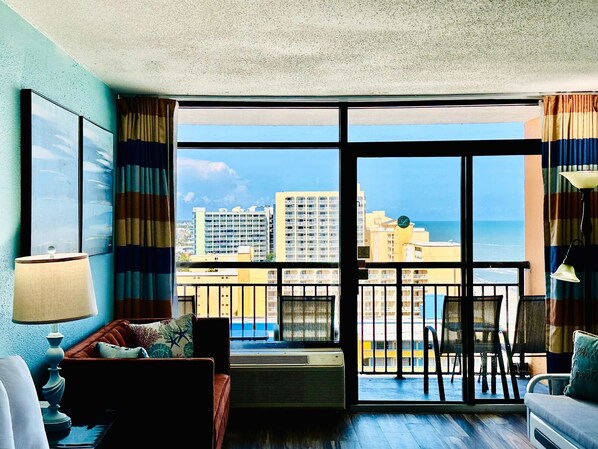 Ein Hotelzimmer mit Balkon, einer Couch, einem Sessel, einem Tisch und Blick auf die Stadt und das Meer.