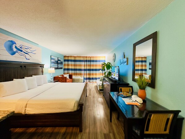 A hotel room with a bed, a desk, a chair, a TV, and a plant.