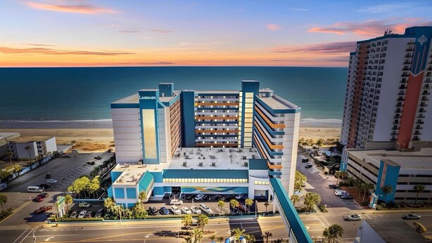 Een meerhoog hotel met een opvallend 'LANDMARK' bord, een parkeerplaats en uitzicht op de oceaan.