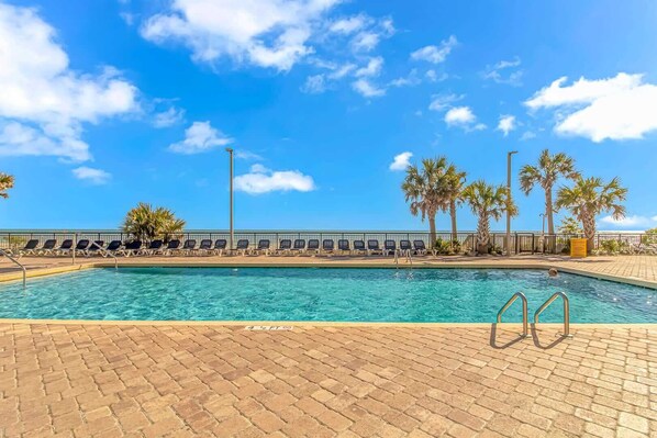 A swimming pool with lounge chairs and palm trees, surrounded by a brick walkway.